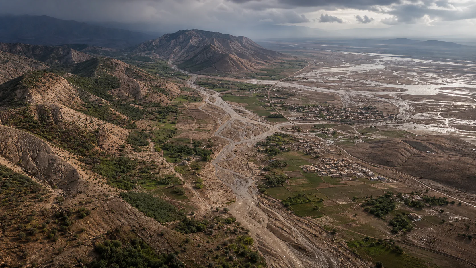 An oblique view of a semi-arid Iranian watershed shows vegetated slopes, converted farmland, settlements, and runoff channels converging on a floodplain.