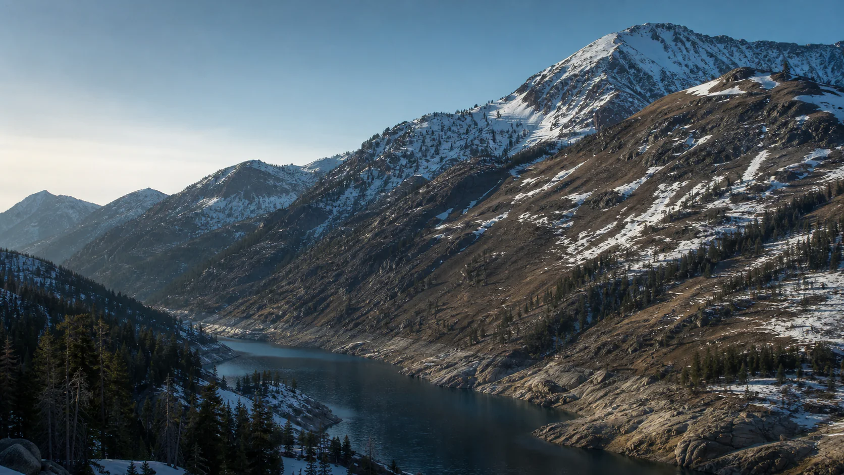 Sparse snow covers a western U.S. mountain watershed above a narrow reservoir, illustrating reduced seasonal water storage.
