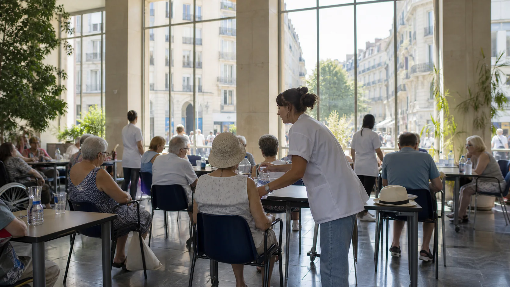 Health workers distribute water to older residents in a bright French urban cooling center during extreme heat.