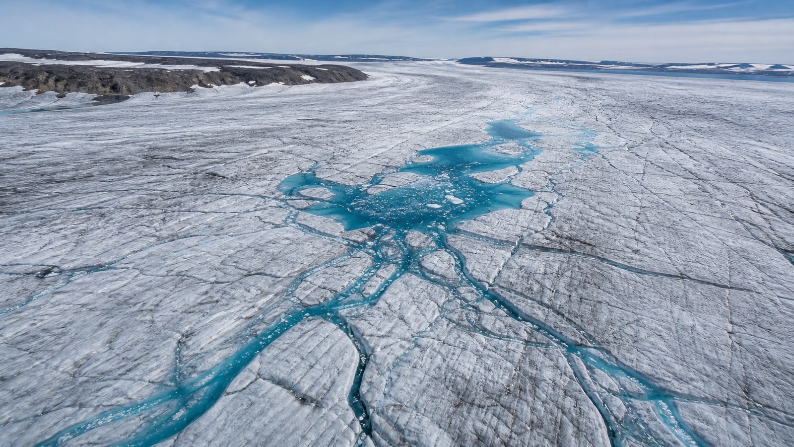 Turquoise meltwater channels spread across exposed ice on Canada's Barnes Ice Cap.