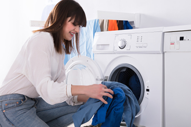 Woman loads a washing machine during daytime, illustrating free midday electricity use.