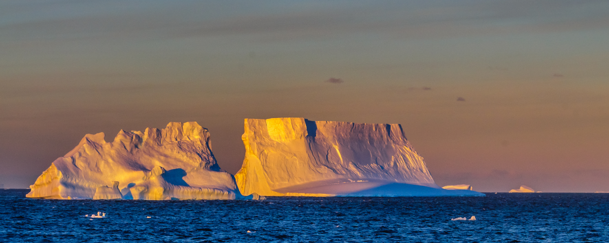 Sunlit icebergs float in dark blue ocean water.