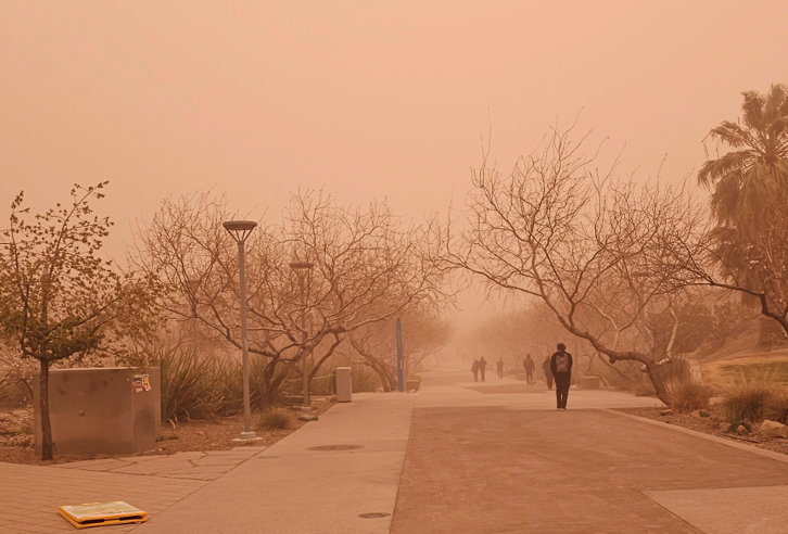 People walk through orange dust during a severe sand and dust storm.